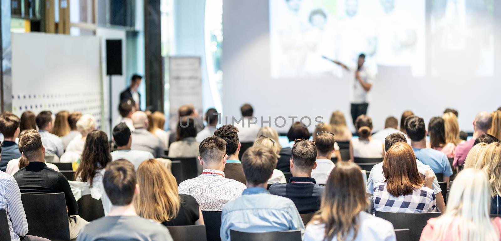 Speaker giving a talk in conference hall at business event. Audience at the conference hall. Business and Entrepreneurship concept. Focus on unrecognizable people in audience.