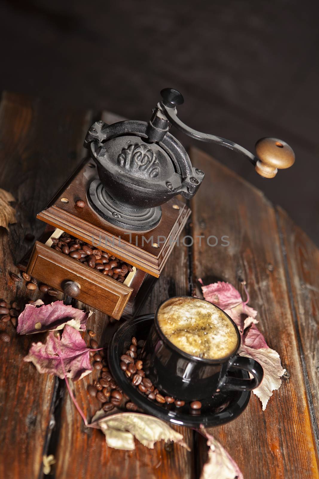 Coffee mill, beans, cup of coffee and autumn leaves on a wooden desk