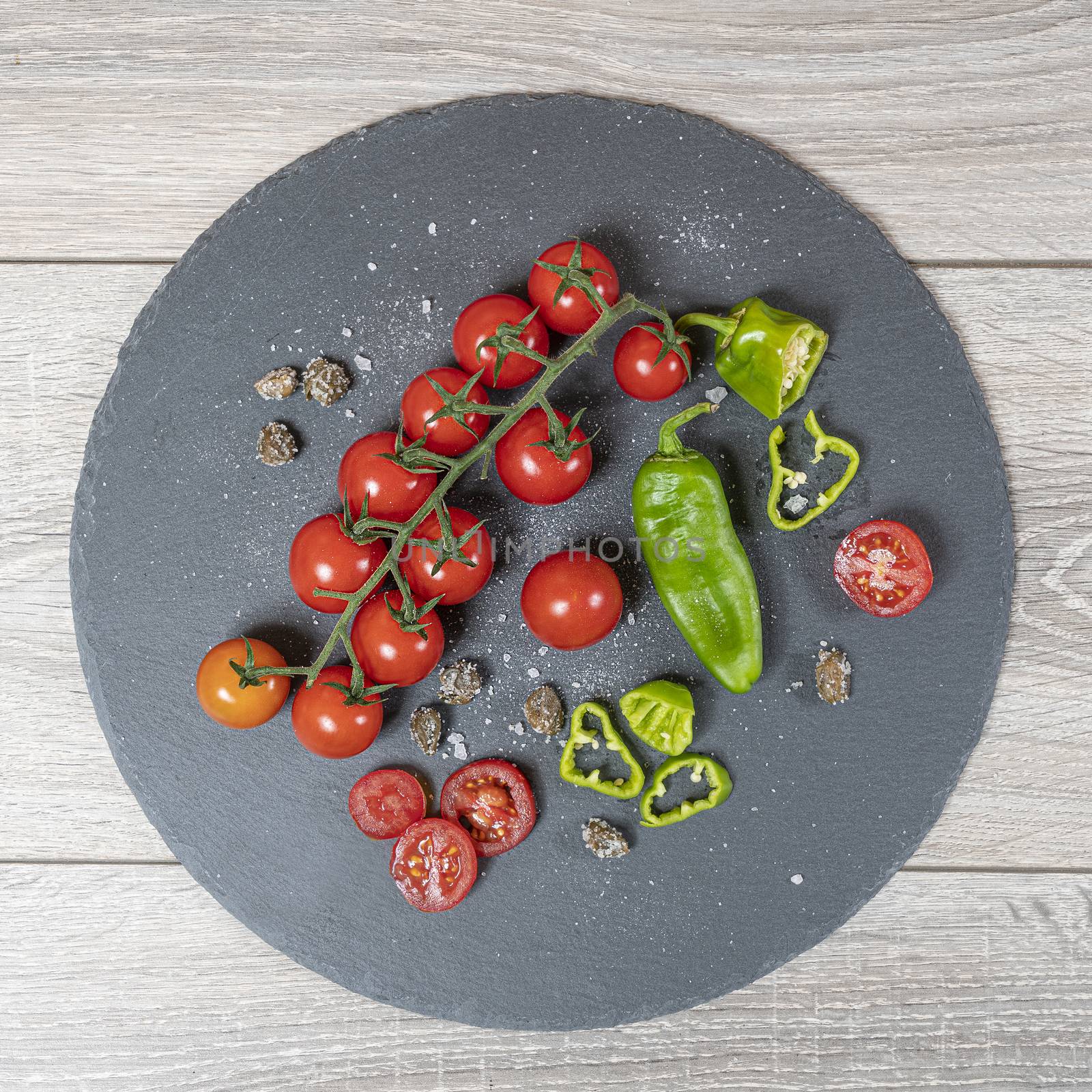 some small tomatoes and green peppers on a stone plate