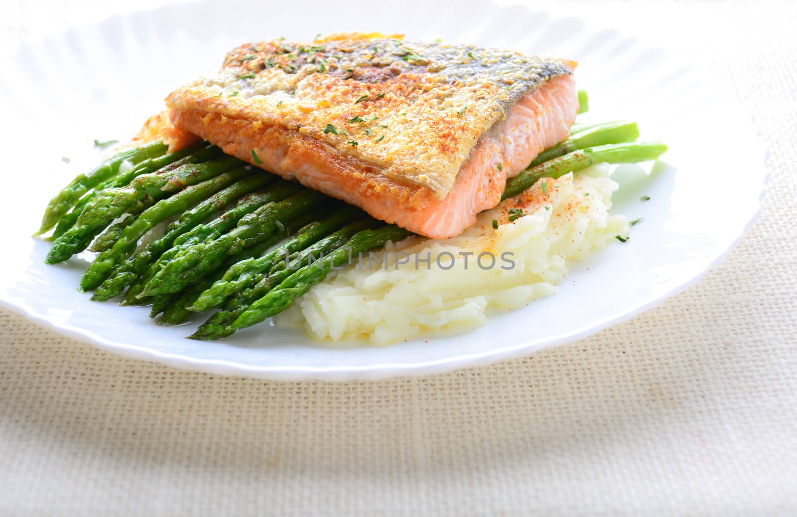 Grilled salmon garnished with asparagus and herbs and mashed potatoes, served on white plated.
