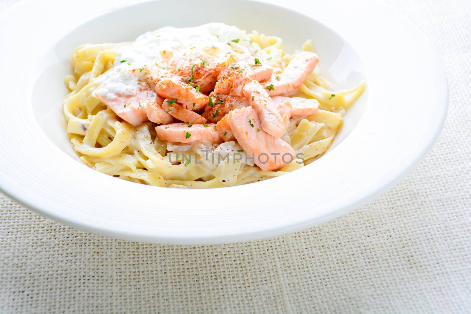 Fettucine with salmon, egg and parmesan cheese, served on white plate.
