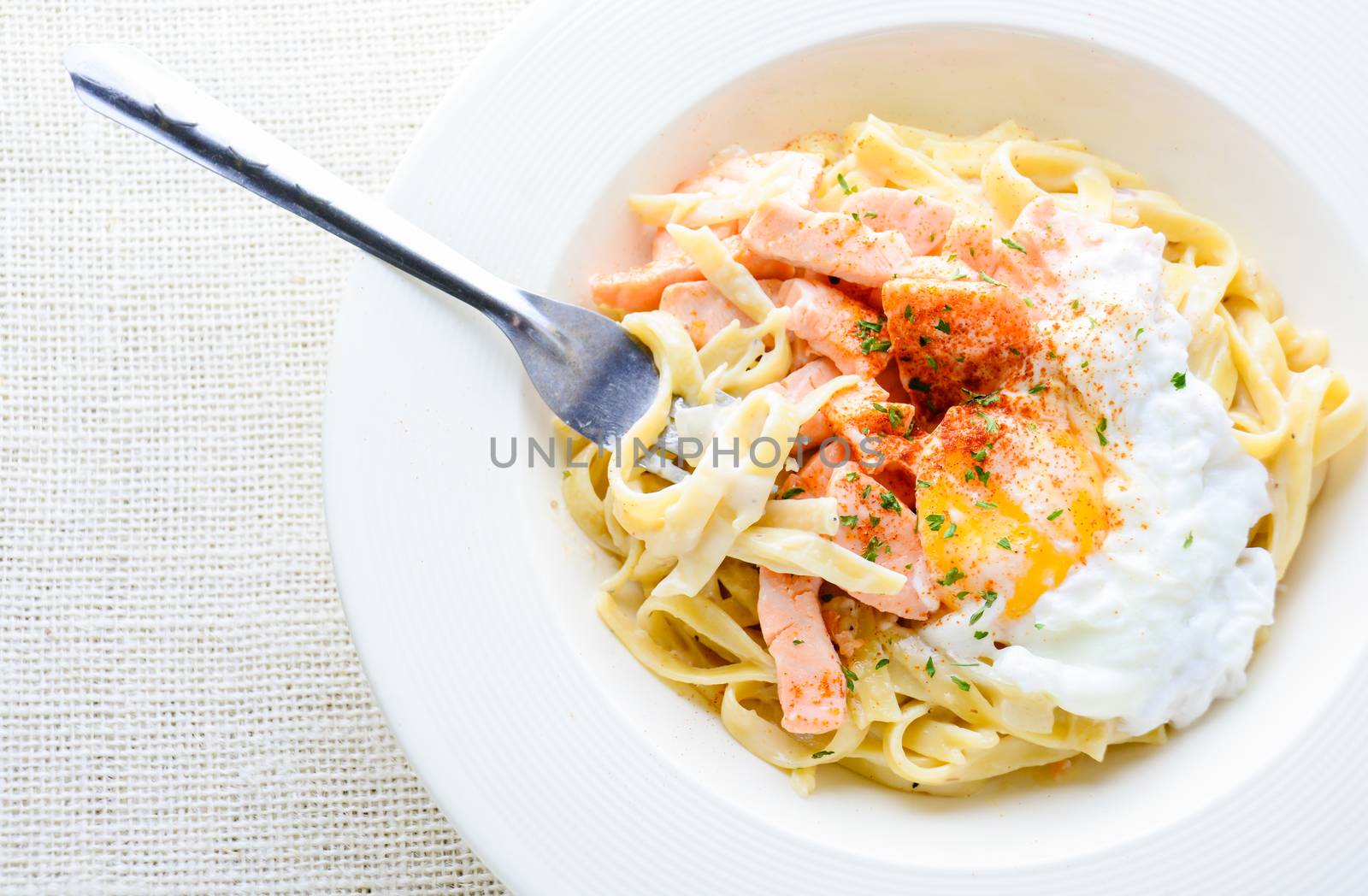 Fettucine with salmon, egg and parmesan cheese, served on white plate.
