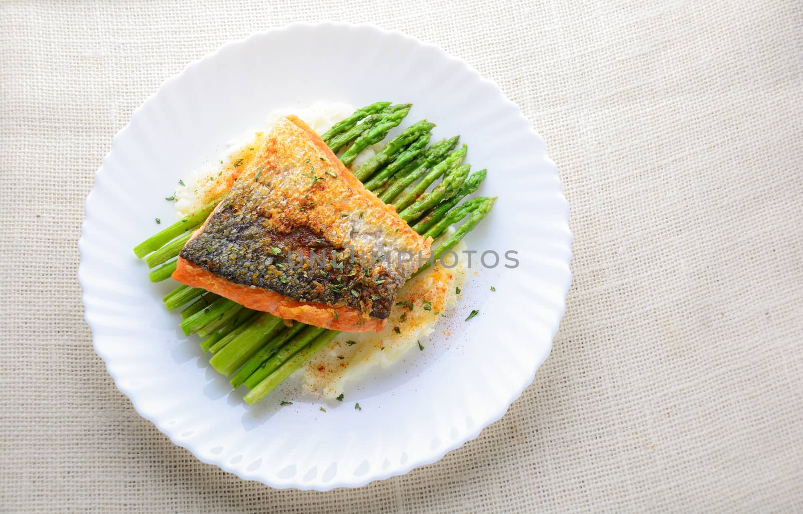 Grilled salmon garnished with asparagus and herbs and mashed potatoes, served on white plated.
