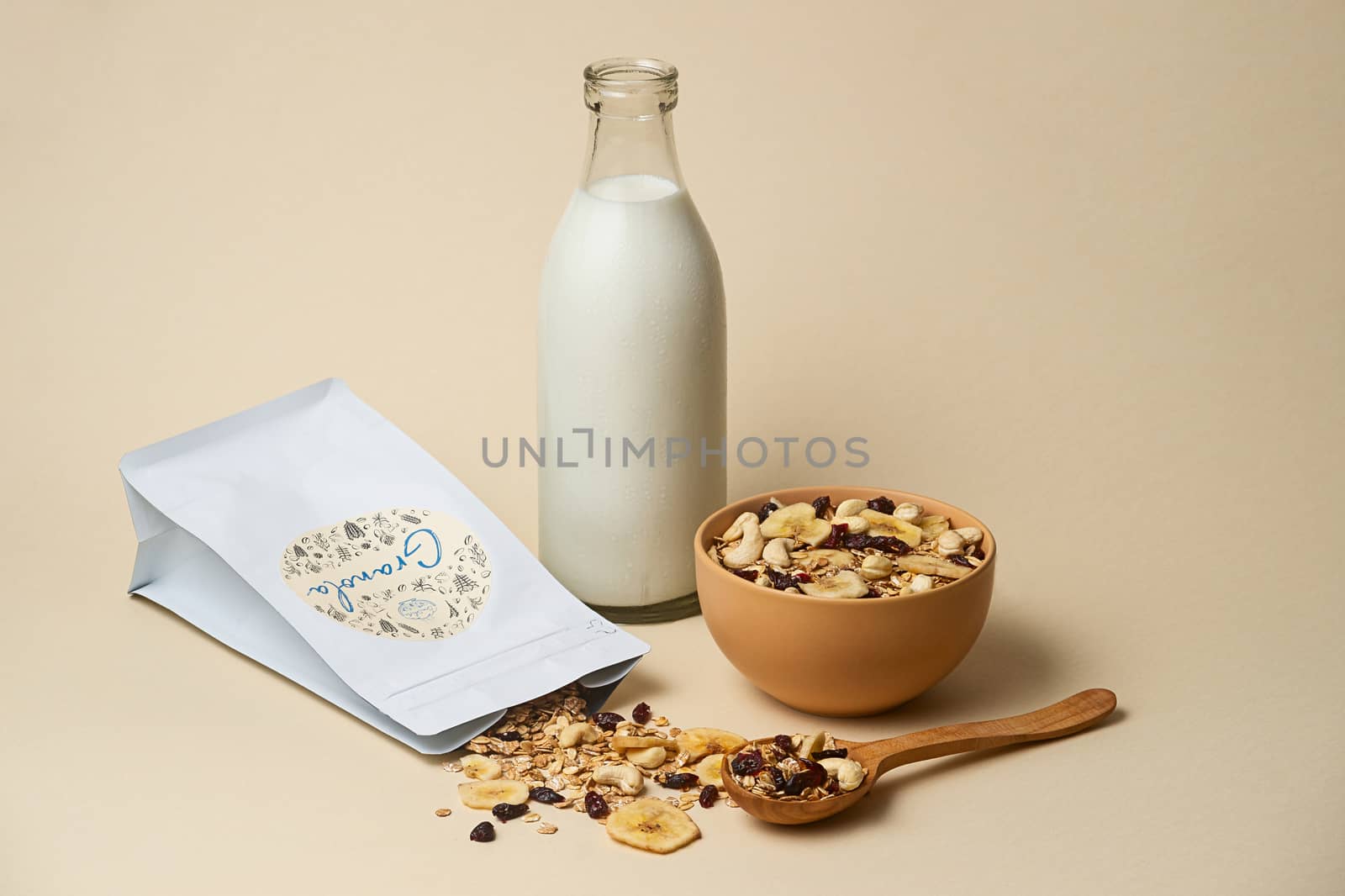 06.19.2019 Kyiv, Ukraine.Nutrition concept. The bowl of granola with  milk bottle, wooden spoon and granola package on beige colour background. Very big depth of field. Granola stock photo. 