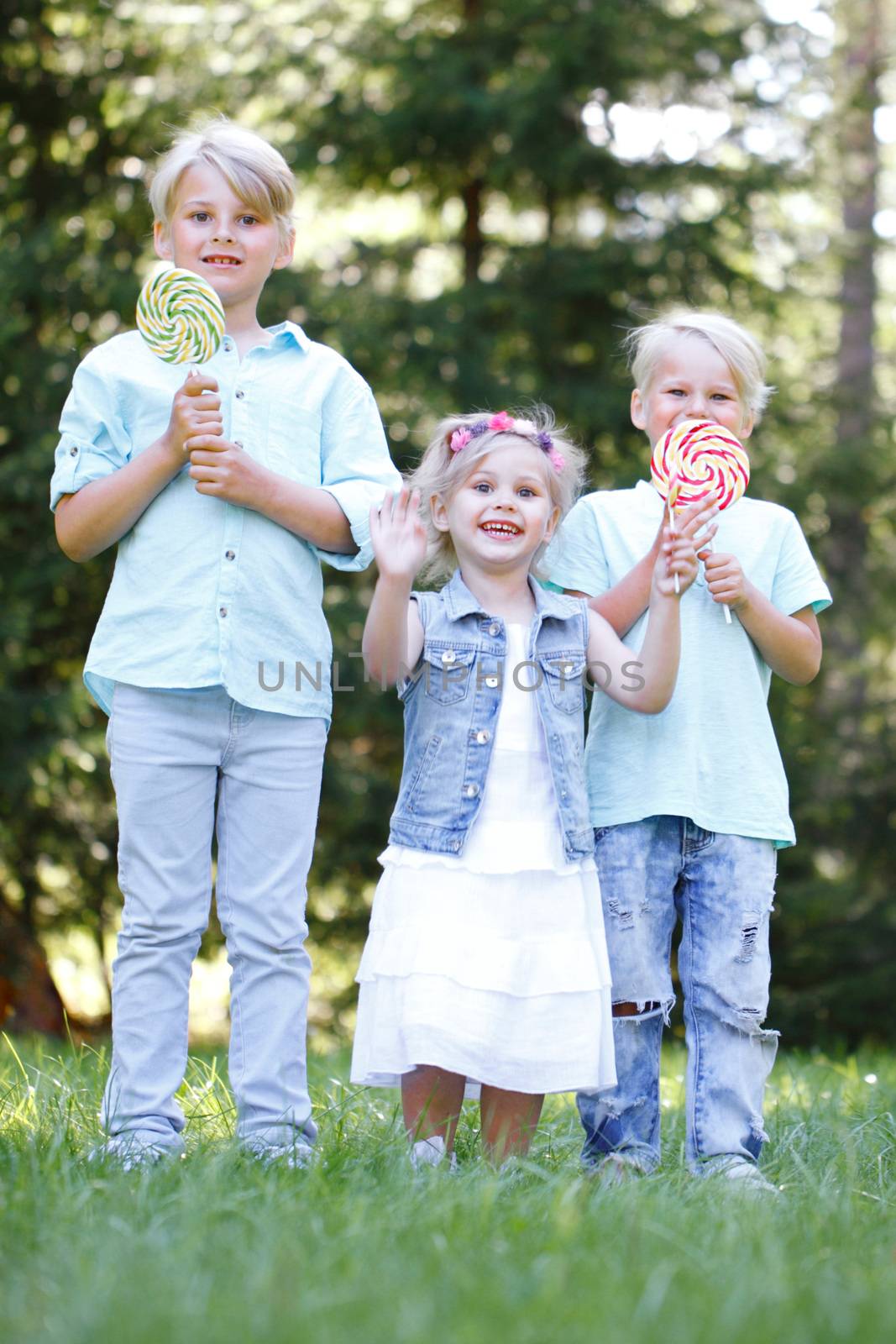 Group of happy children eating lollipops outdoors in summer park