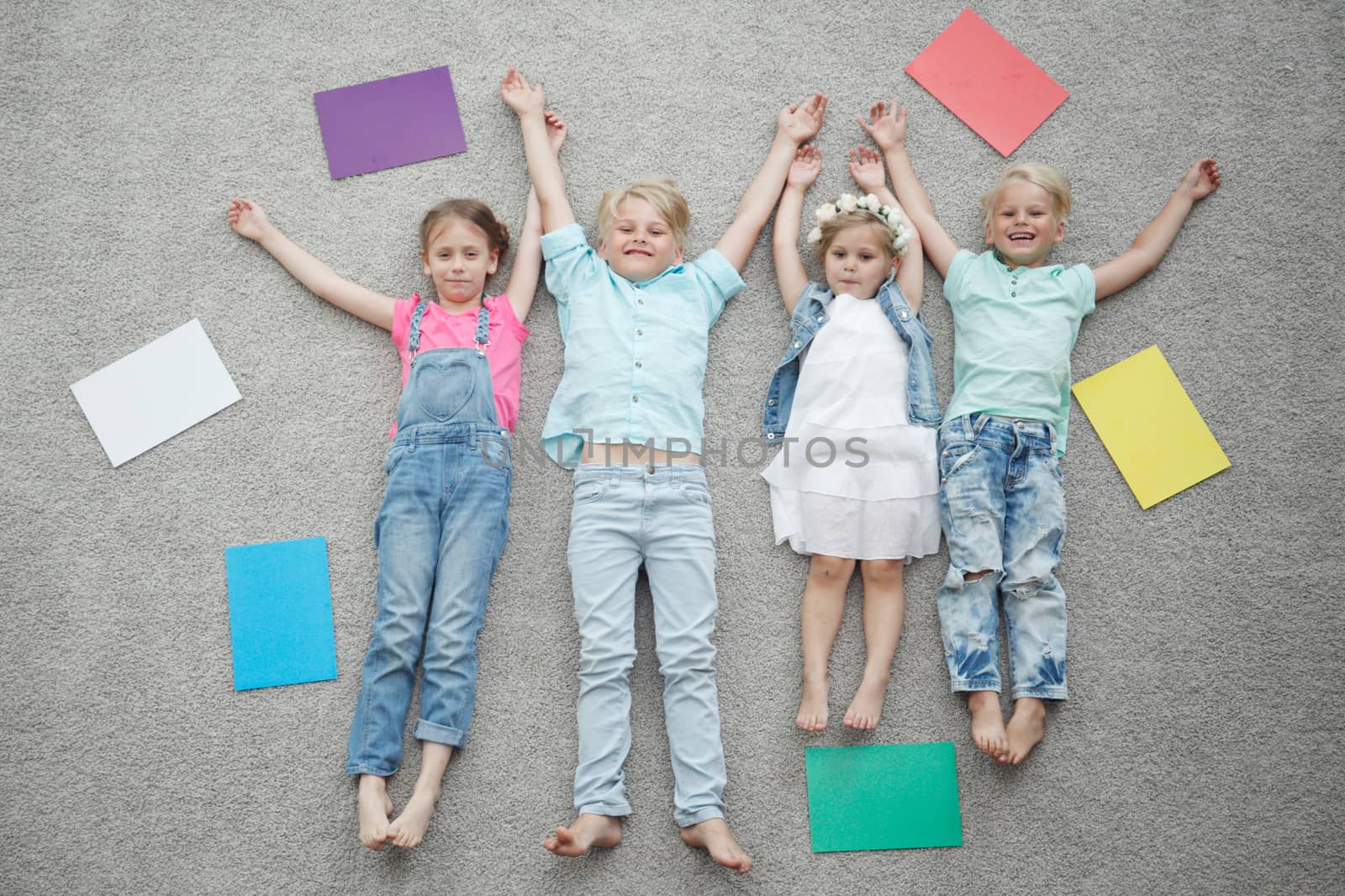 Four happy children laying on floor and smiling among colorful paper