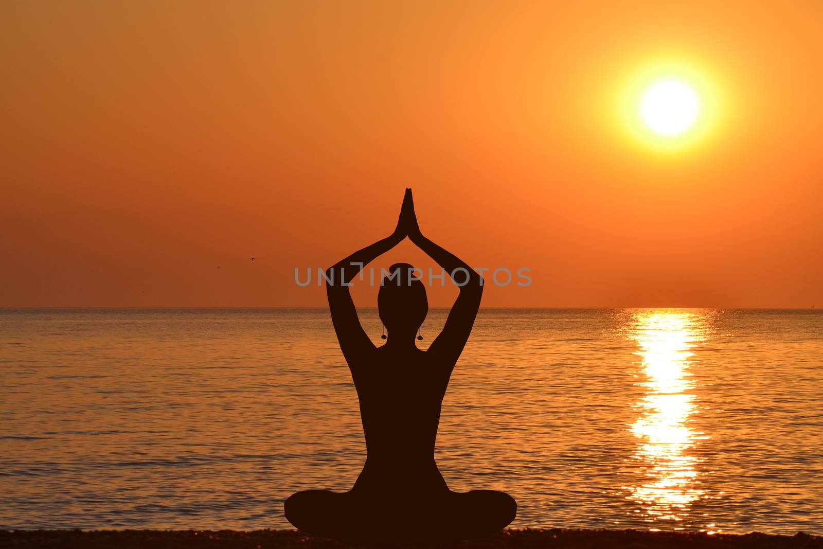 Silhouette of young woman practicing yoga on the beach at sunris by hibrida13