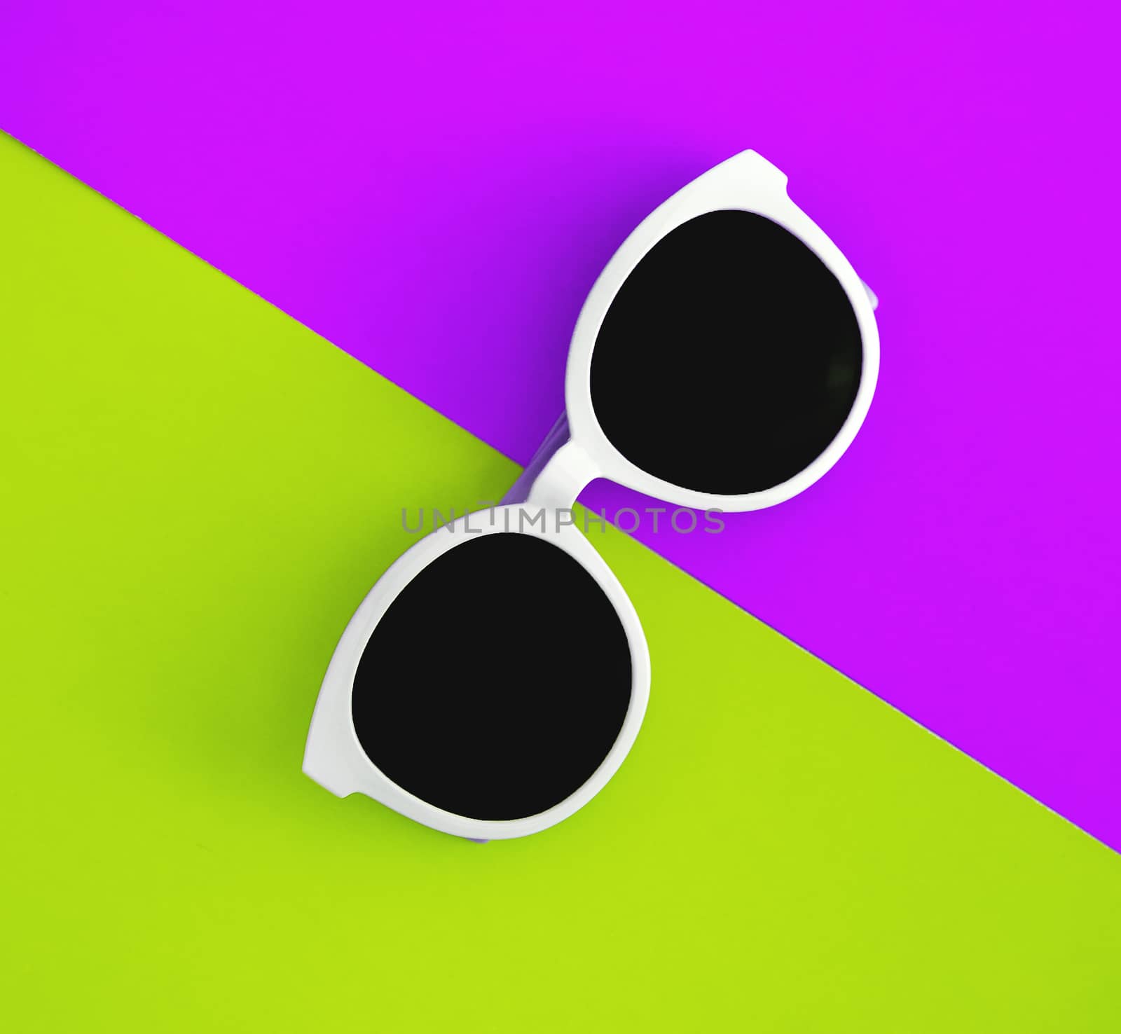 Sunny stylish white sunglasses on a bright purple-lilac and yellow-green background, top view, isolated. Copy space. Flat lay.