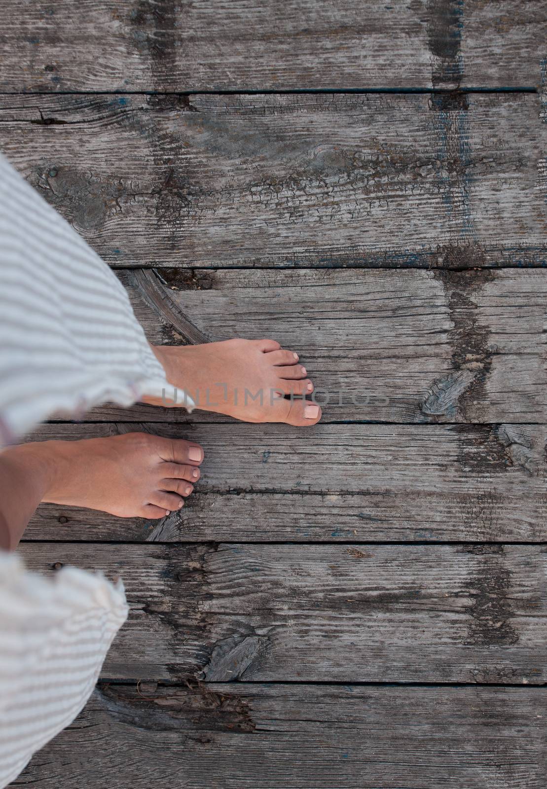 Beautiful female bare bare tanned legs with pink pedicure on wooden beach flooring. Top view, copy space.