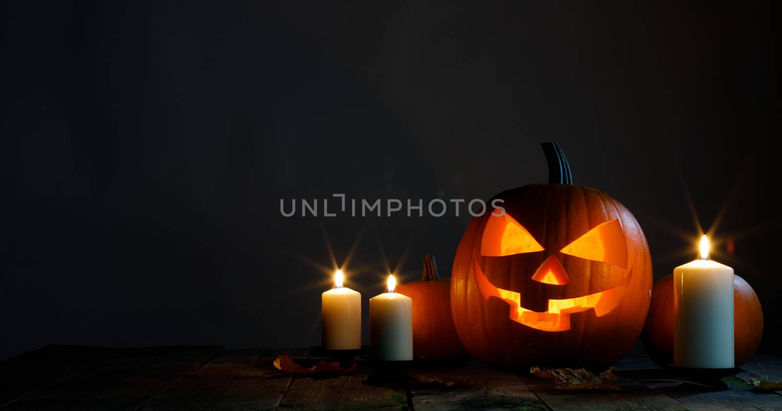Halloween pumpkin head jack o lantern candles and dry maple leaves on wooden background