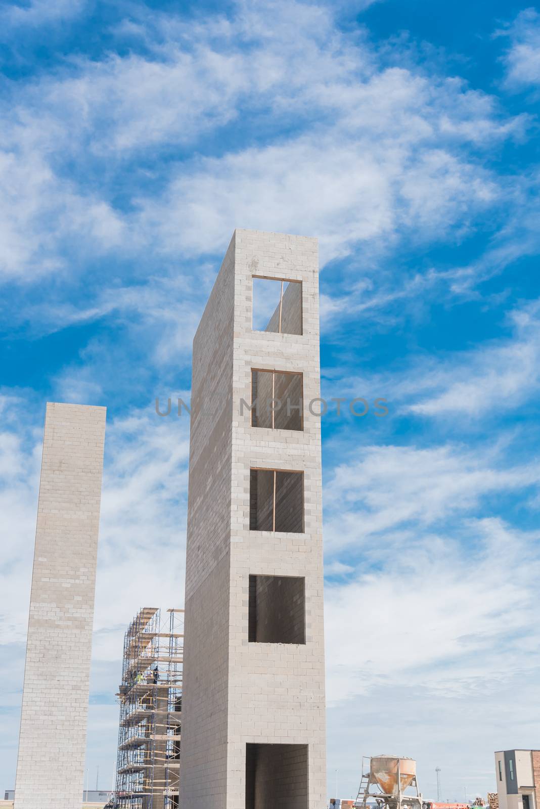Typical construction site of new condominium building in Texas, America with elevator shaft and metal scaffolding system. Looking up view of concrete elevator tower under cloud blue sky