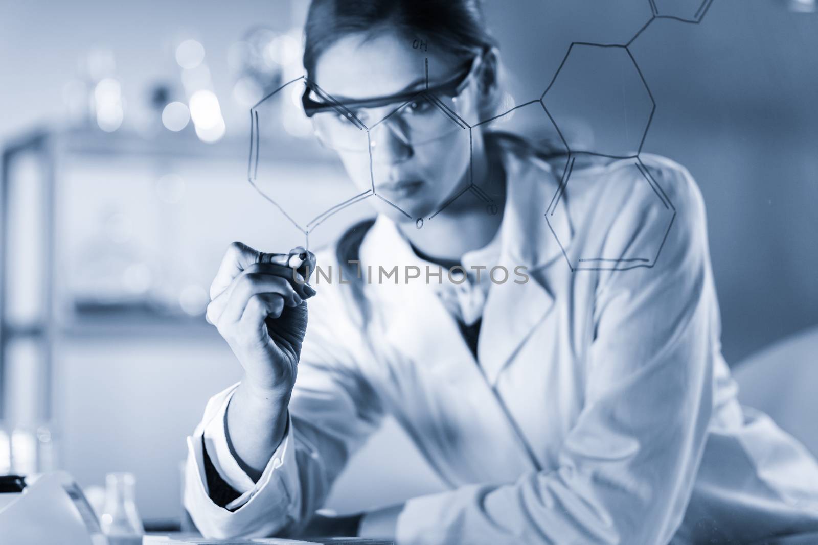 Portrait of a confident female researcher in life science laboratory writing structural chemical formula on a glass board. by kasto