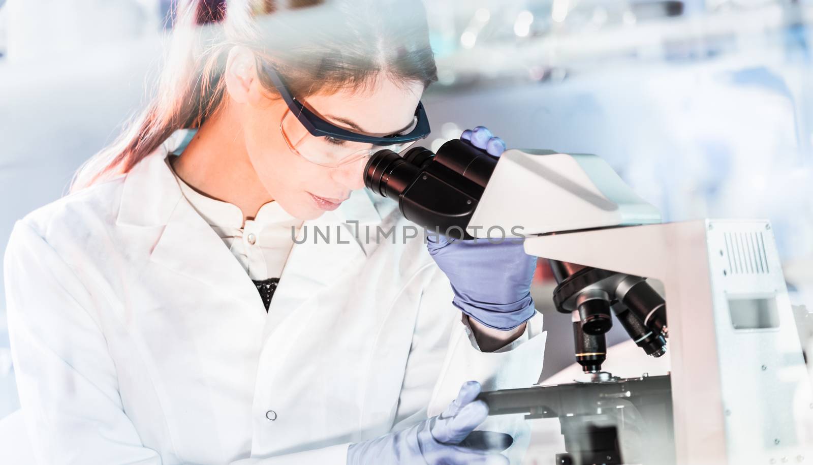 Life scientists researching in laboratory. Focused female young scientist microscoping in scientific working environment. Healthcare science and biotechnology.