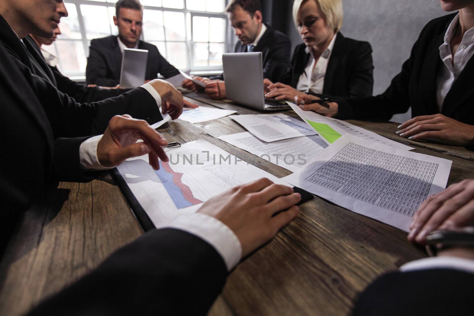 Group of diverse business executives holding a meeting around a table discussing graphs charts showing statistical data analysis