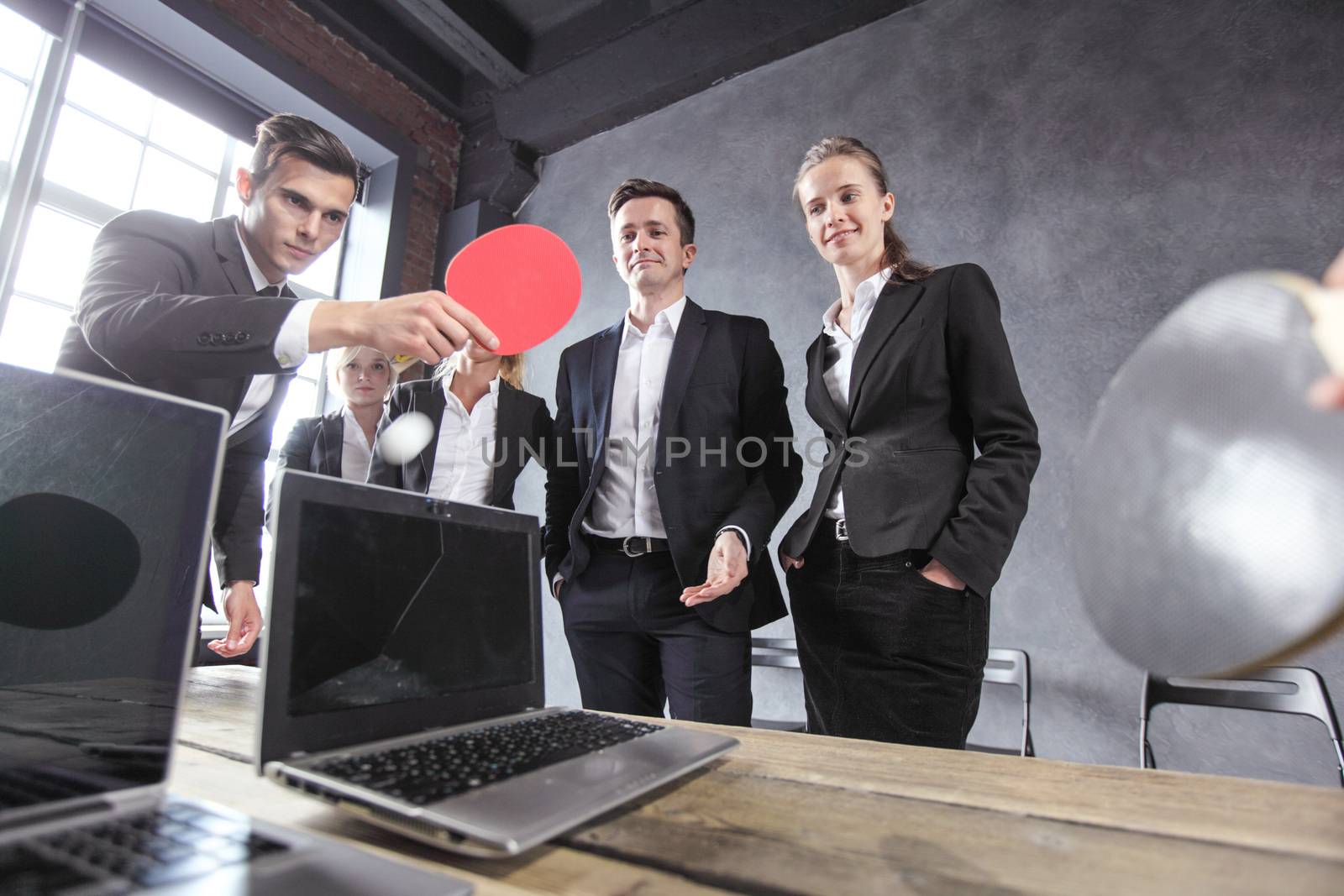 Business people play ping pong on office table with laptops