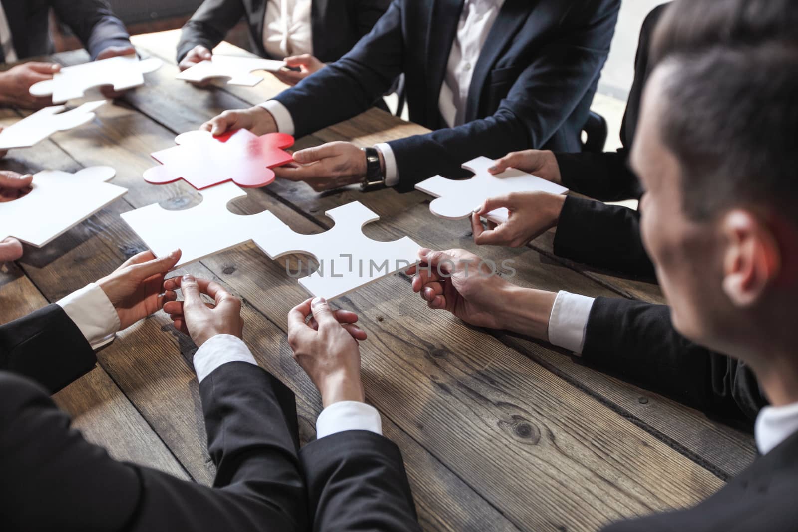 Business people and puzzle on wooden table, teamwork concept
