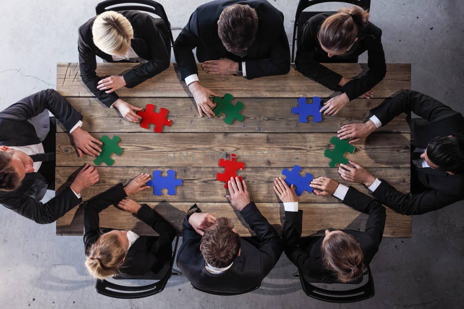 Business people and puzzle on wooden table, teamwork concept