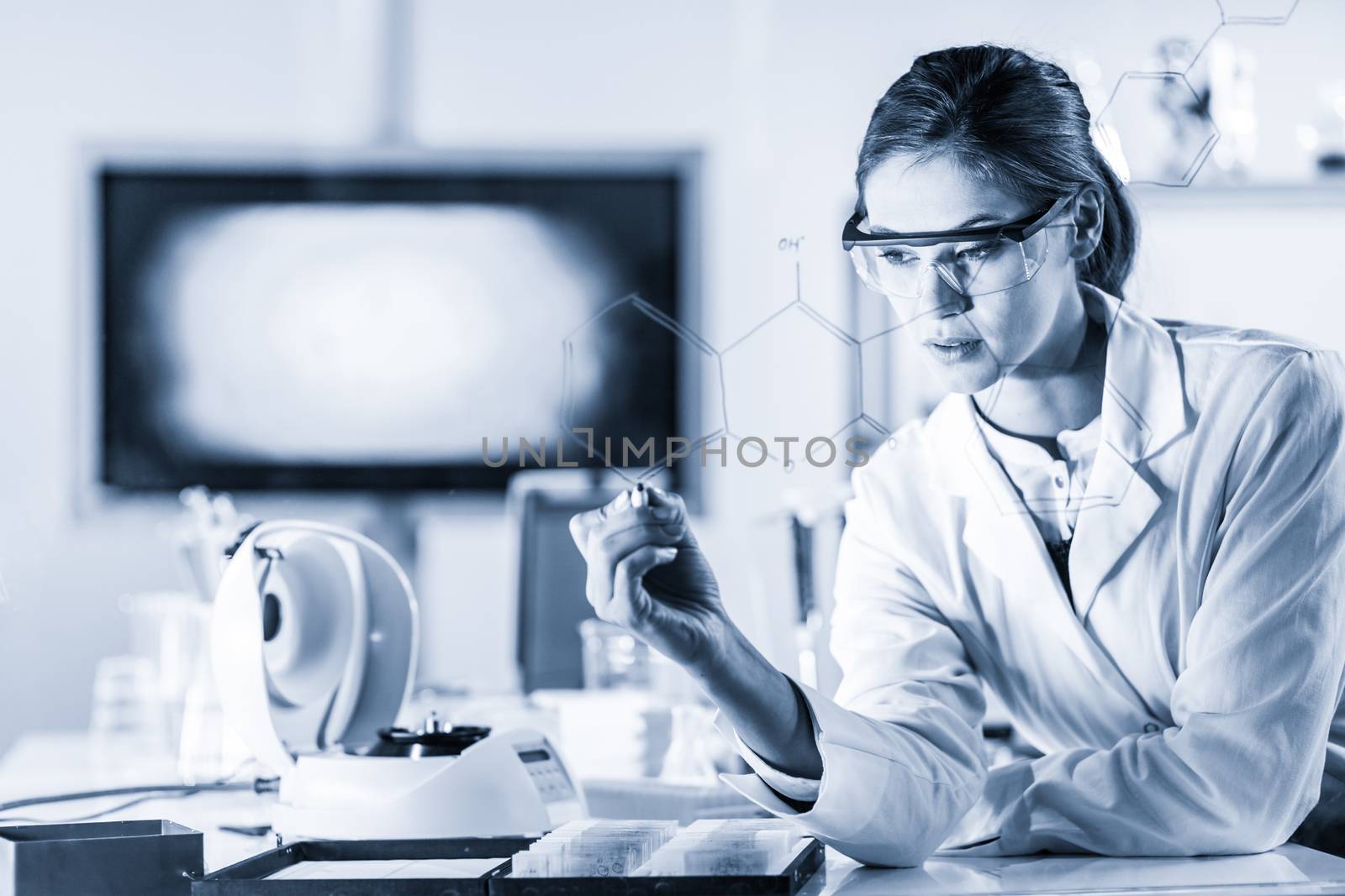 Portrait of a confident female health care expert in life science laboratory writing structural chemical formula on a glass board. Healthcare and modern life science concept. Blue toned image.