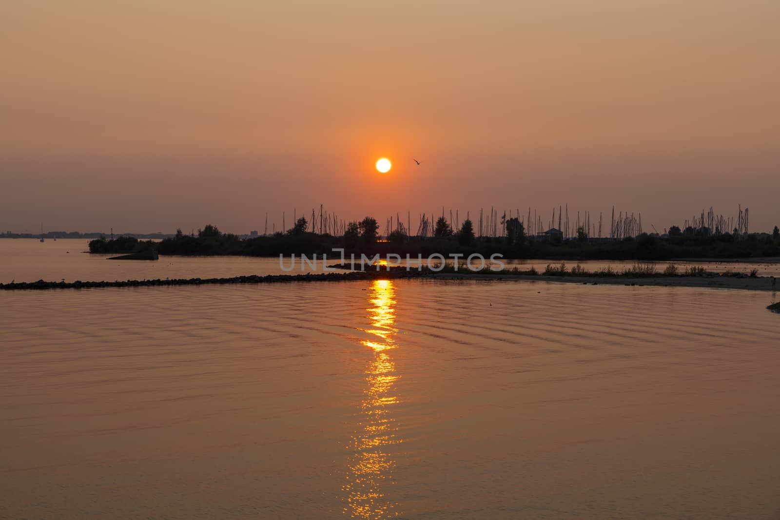 sunset over the harbor of Hellevoetsluis with the boats with masts in silhouette as background and the sky orange red