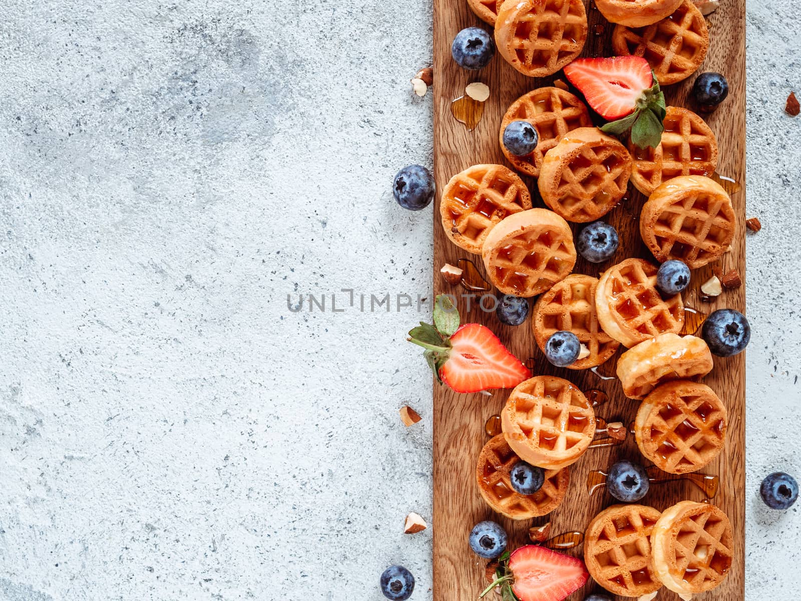 Small round delicious soft belgian waffles on cutting board. Fresh belgian waffles with berries and caramel sauce top view. Copy space for text or mock up
