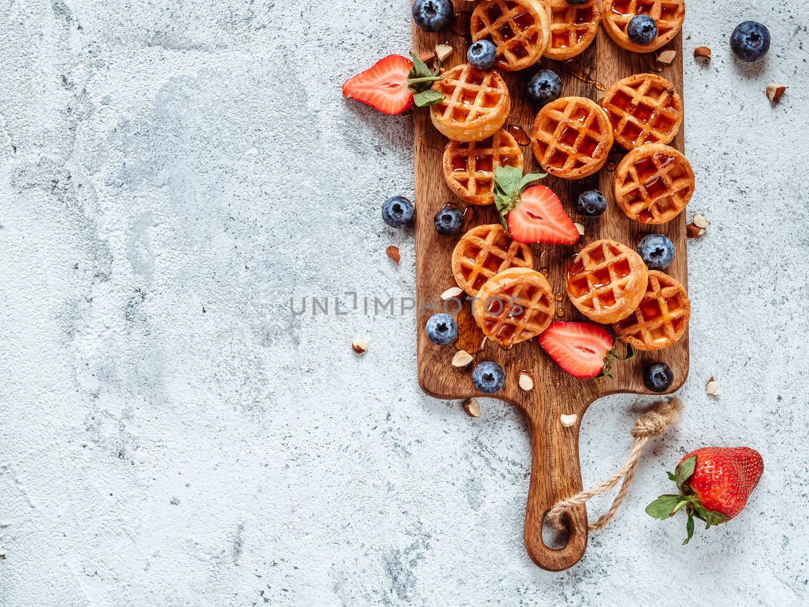 Small round delicious soft belgian waffles on cutting board. Fresh belgian waffles with berries and caramel sauce top view. Copy space for text or mock up