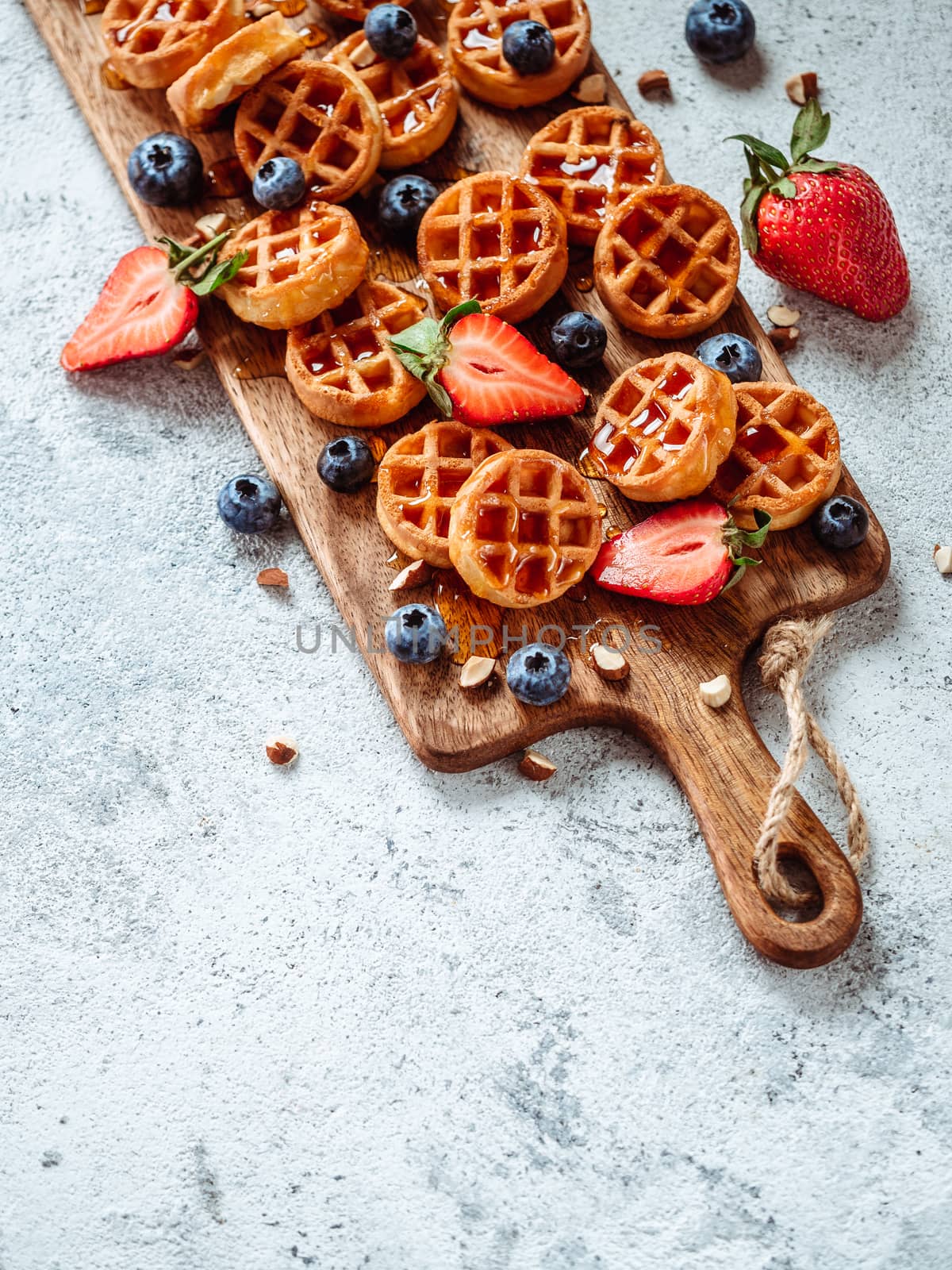 Small round delicious soft belgian waffles on cutting board. Fresh belgian waffles with berries and caramel sauce top view. Copy space for text or mock up. Vertical