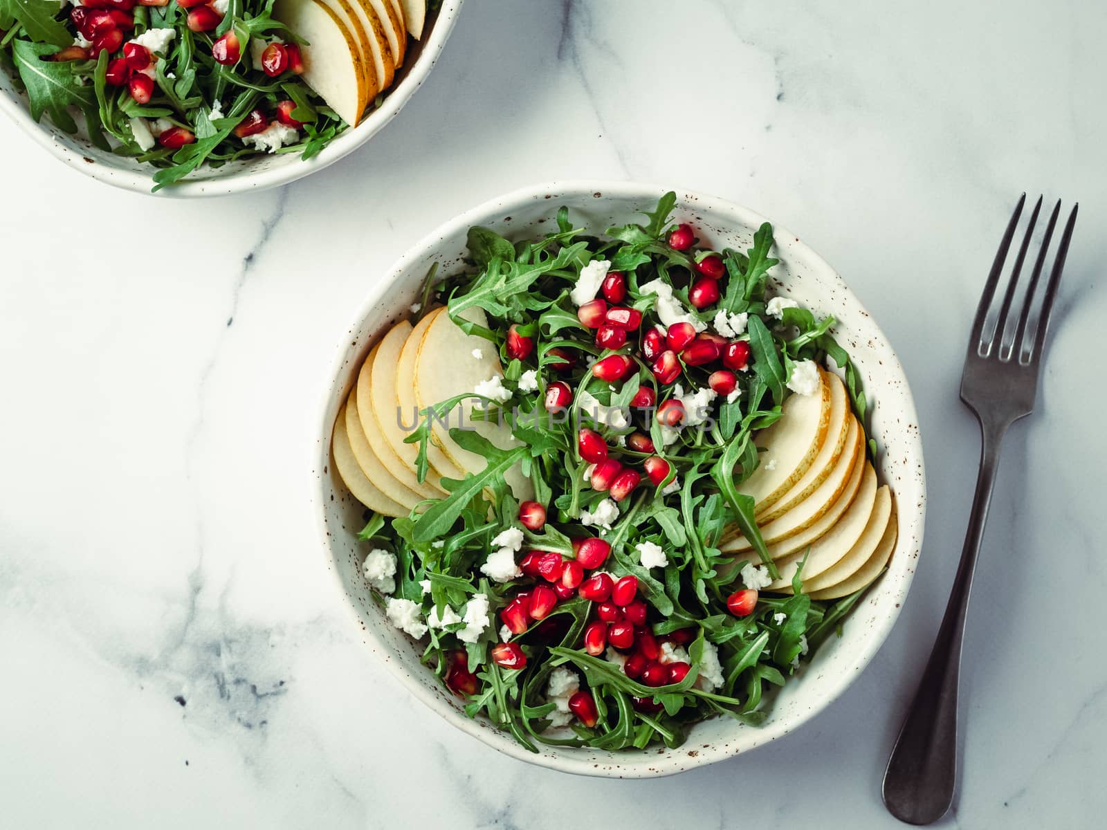 Vegan salad bowl with arugula, pear, pomegranate, coconut crumble or cottage cheese on marble tabletop. Vegan breakfast, vegetarian food, diet concept. Top view or flat lay.