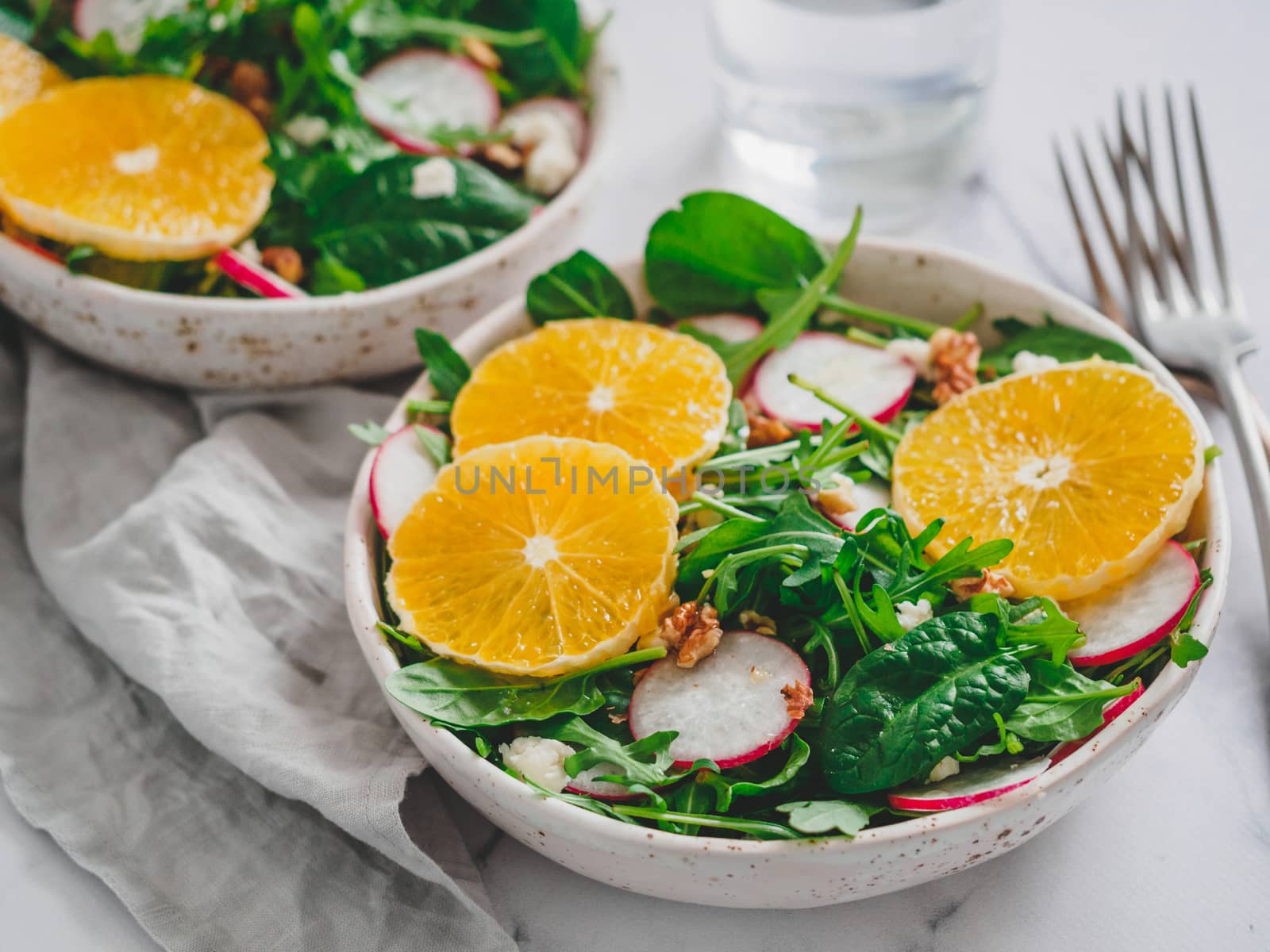 Vegan salad bowl with oranges, spinach, arugula, radish, nut. Top view. Vegan breakfast, vegetarian food, diet concept. Two bowls with salad on white marble tabletop