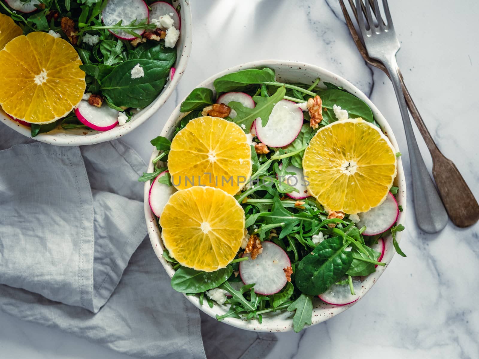 Vegan salad bowl with oranges, spinach, arugula, radish, nut. Top view. Vegan breakfast, vegetarian food, diet concept. Two bowls with salad on white marble tabletop