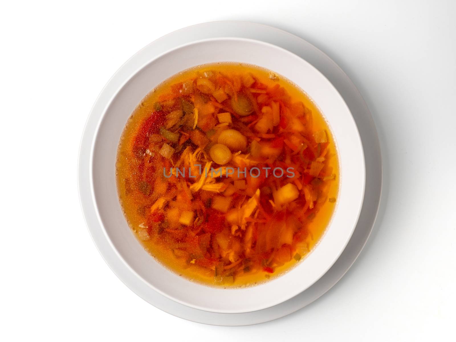 Bowl with chicken, beetroot and other vegetables soup. Perfect bright broth in italian minestrone style, isolated on white. Top view or flat lay.