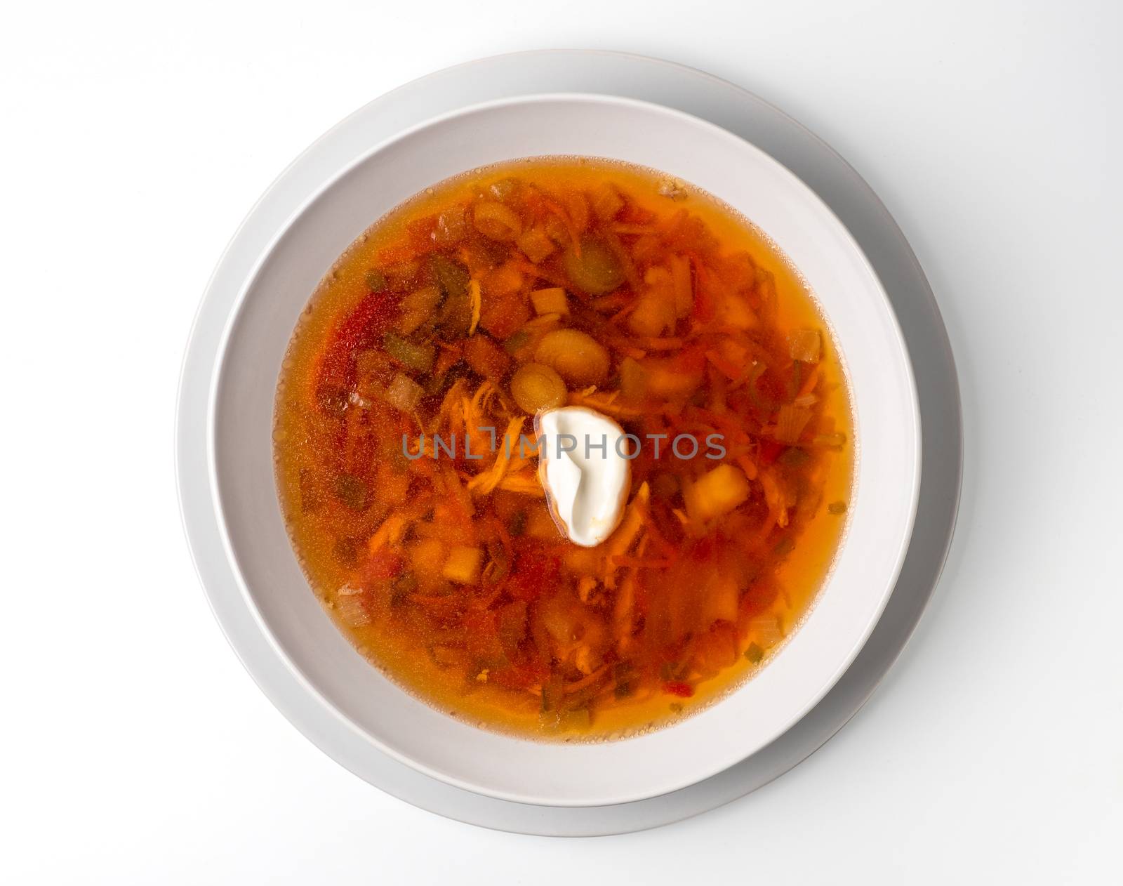 Bowl with chicken, beetroot and other vegetables soup. Perfect bright broth in italian minestrone style, isolated on white. Top view or flat lay.