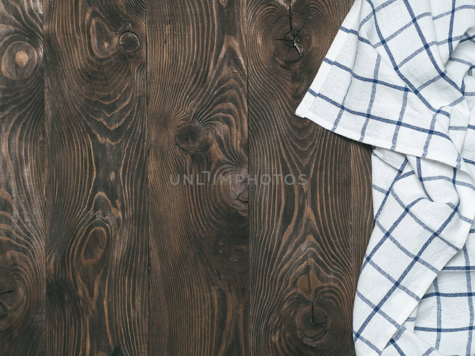 View from above on brown wooden table with linen kitchen towel or textile napkin. Blue tablecloth on dark brown wood tabletop. Copy space for text. Can use as mock up for design