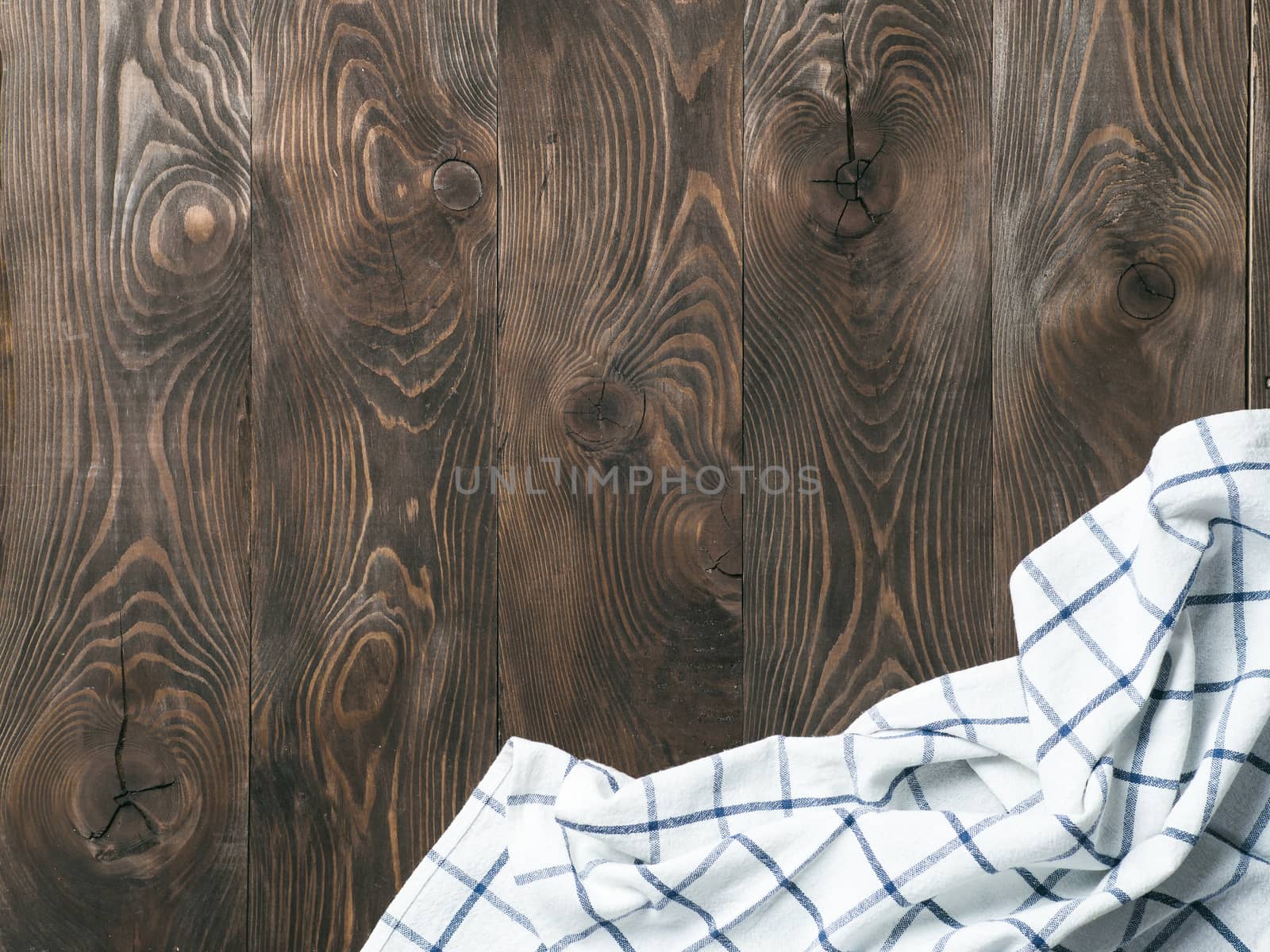 View from above on brown wooden table with linen kitchen towel or textile napkin. Blue tablecloth on dark brown wood tabletop. Copy space for text. Can use as mock up for design