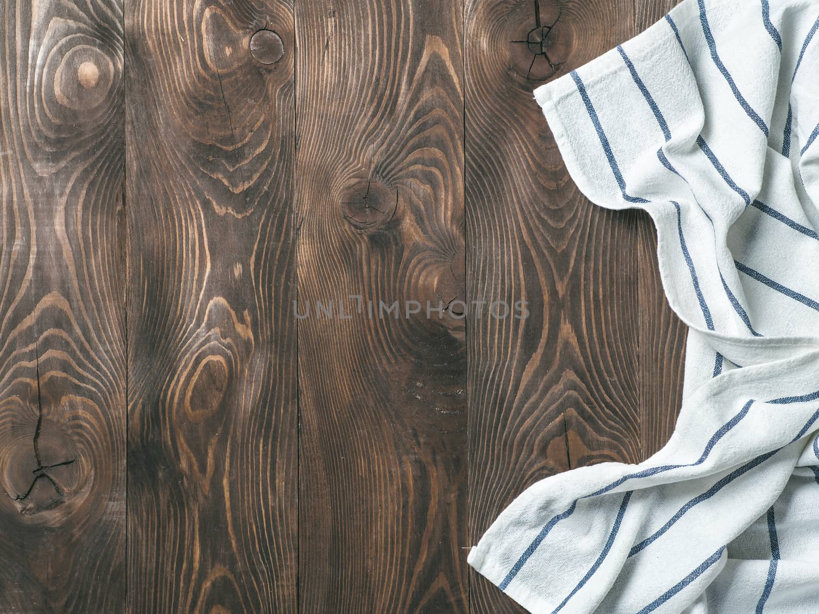 View from above on brown wooden table with linen kitchen towel or textile napkin. Blue tablecloth on dark brown wood tabletop. Copy space for text. Can use as mock up for design