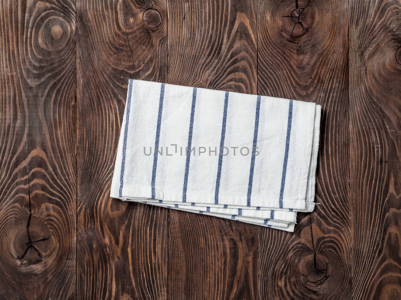 View from above on brown wooden table with linen kitchen towel or textile napkin. Blue folded tablecloth on dark brown wood tabletop. Copy space for text. Can use as mock up for design