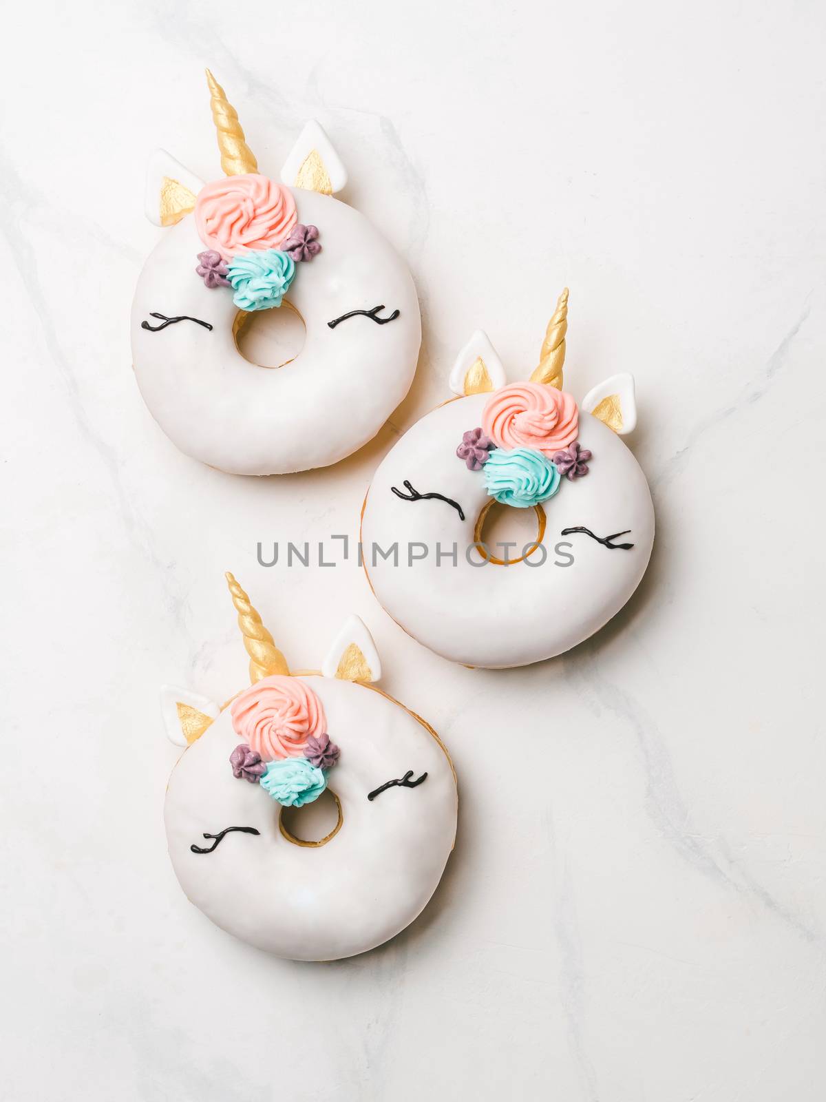 Unicorn donuts over white marble background. Trendy donut unicorn with white glaze. Top view or flat lay. Copy space for text. Vertical.