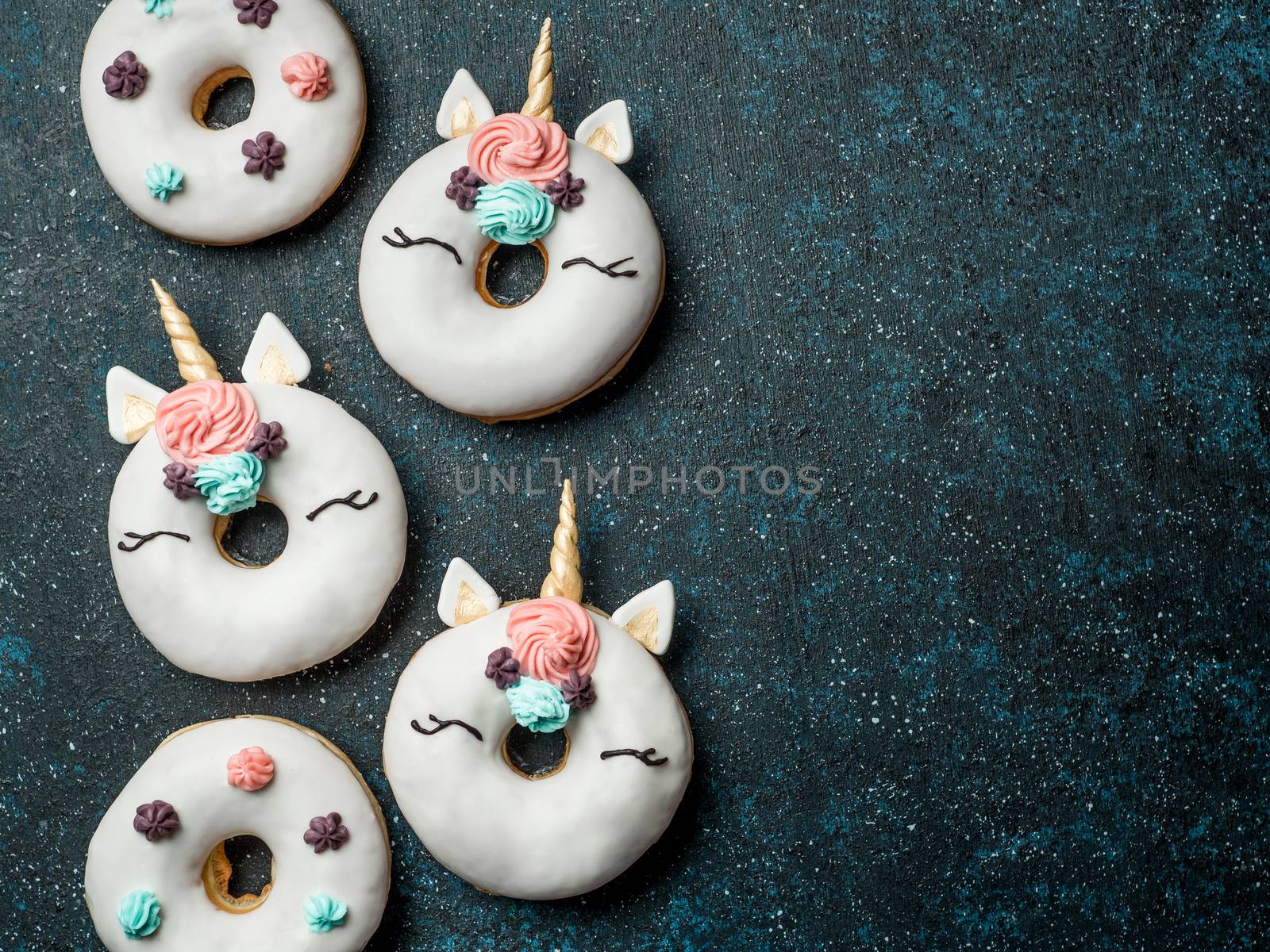 Unicorn donuts over dark background. Trendy donut unicorn with white glaze. Top view or flat lay. Copy space for text.