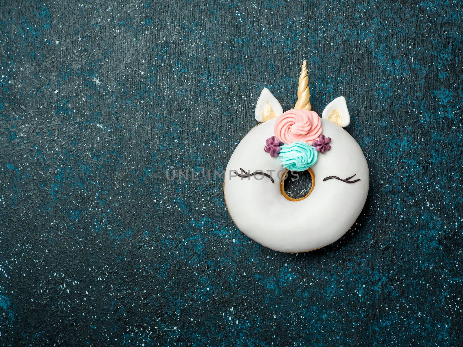 Unicorn donut over dark background. Trendy donut unicorn with white glaze. Top view or flat lay. Copy space for text.