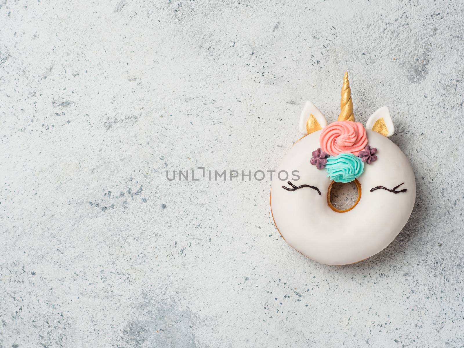 Unicorn donut over gray cement background. Trendy donut unicorn with white glaze. Top view or flat lay. Copy space for text.