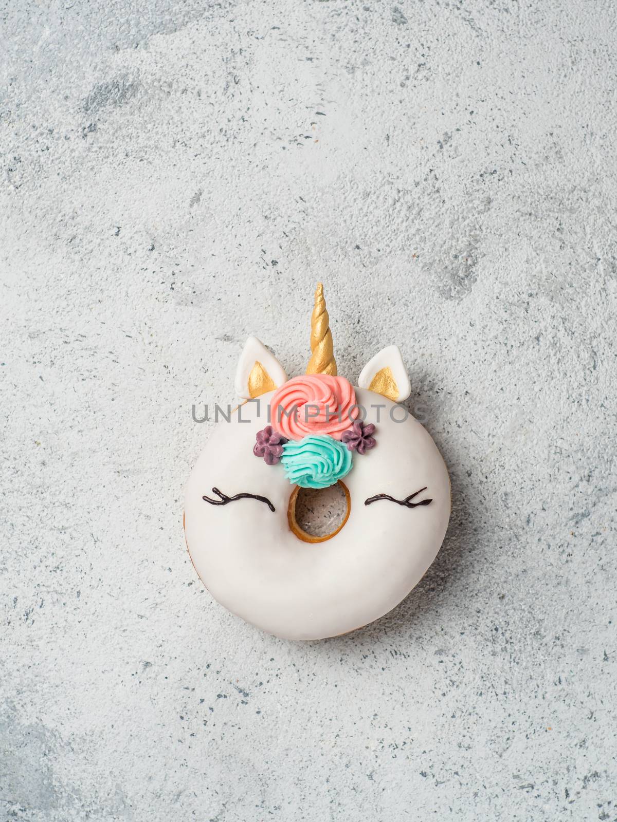 Unicorn donut over gray cement background. Trendy donut unicorn with white glaze. Top view or flat lay. Copy space for text. Vertical.