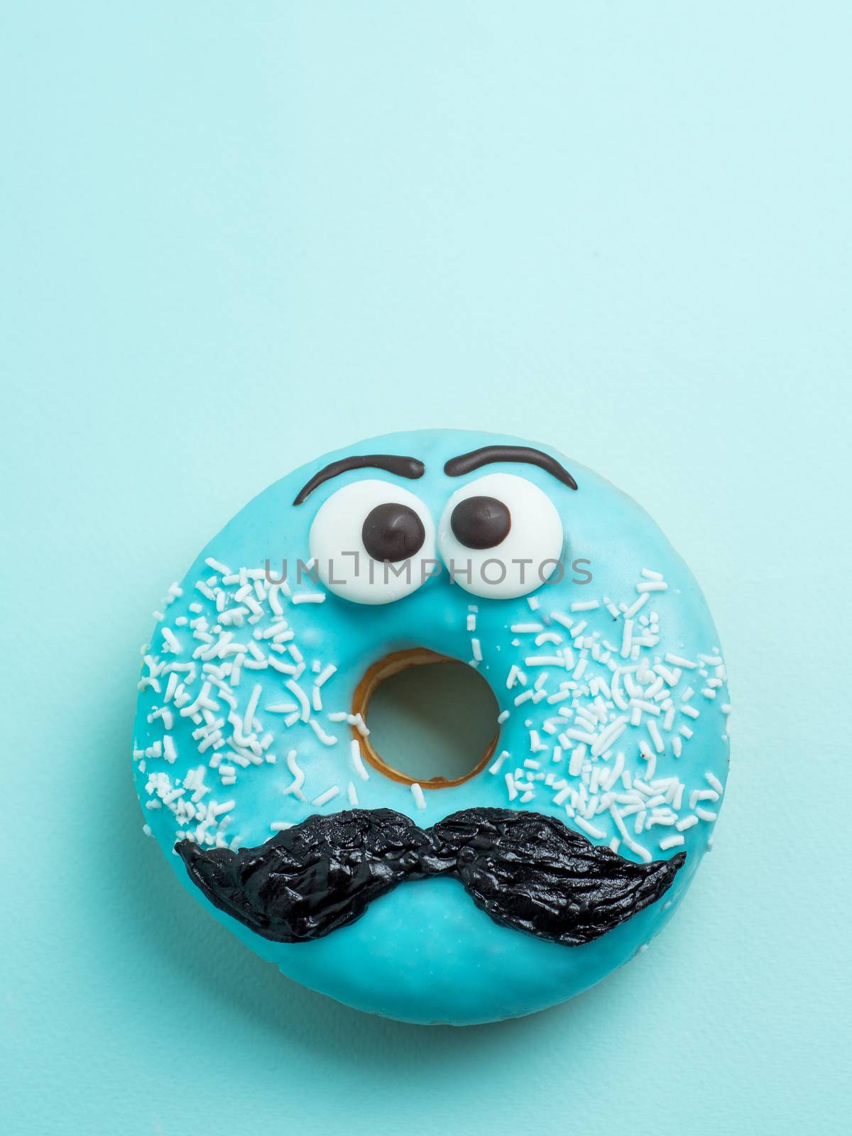 Blue glazed donut with mustache. Blue doughnut with funny face with mustache on blue background. Copy space for text. Masculinity or father day concept. Top view or flat lay. Vertical.