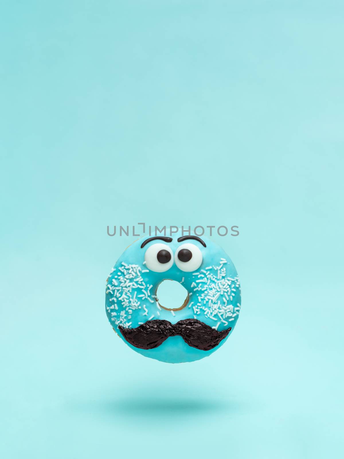 Blue glazed donut with mustache. Flying blue doughnut with funny face with mustache over blue background. Copy space for text. Masculinity or father day concept. Vertical.