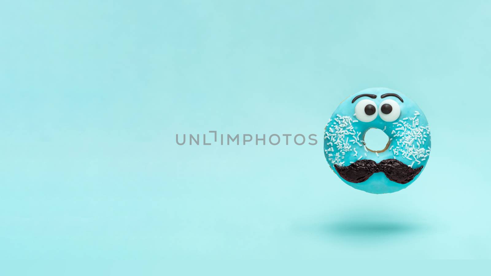 Blue glazed donut with mustache. Flying blue doughnut with funny face with mustache over blue background. Copy space for text. Masculinity or father day concept. Banner