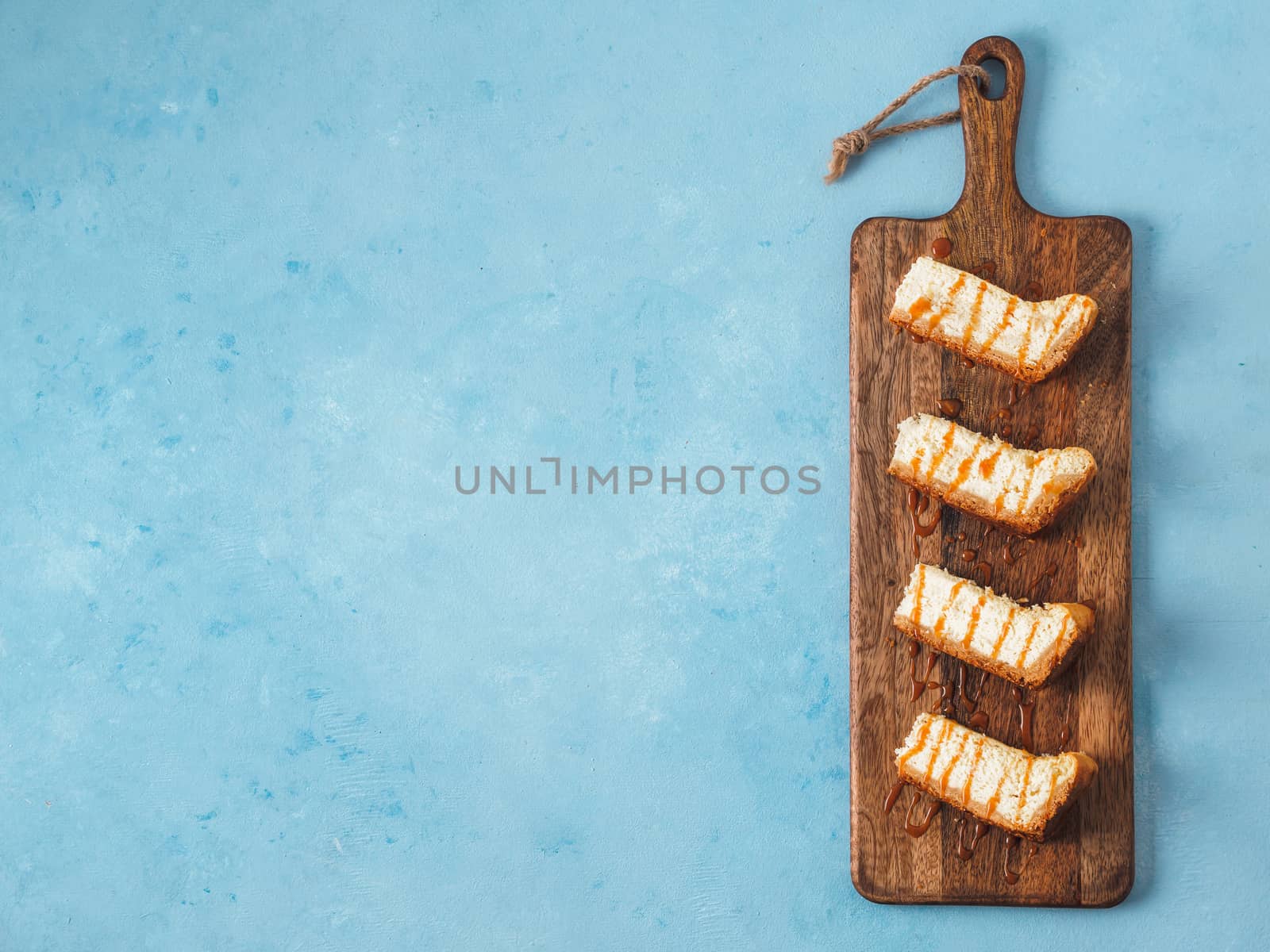 caramelized cheesecake slices on wooden cuttingboard. Cheesecake on blue background with copy space for text. Top view or flat lay.