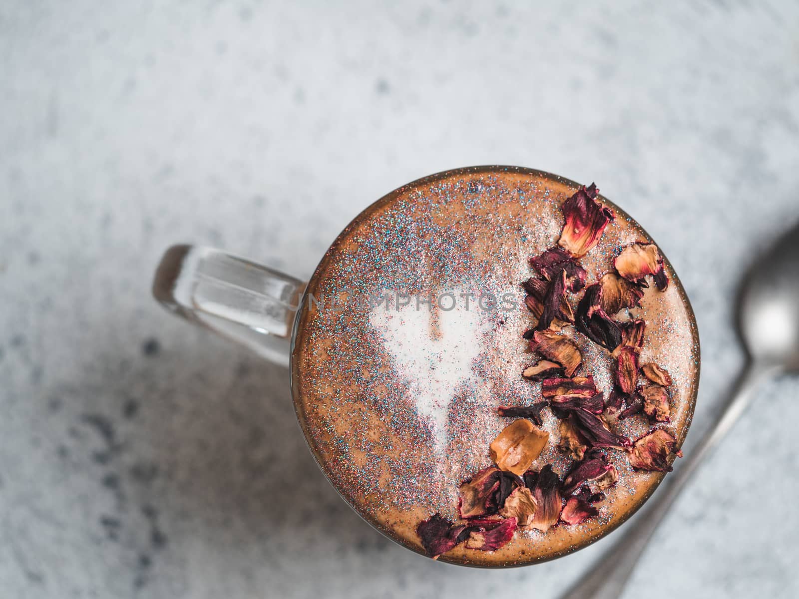 Trendy Coffee with edible glitter and dried rose petals. Cup of sparkly coffee or diamond cappuccino on gray table. Copy space for text. Top view or flat lay.