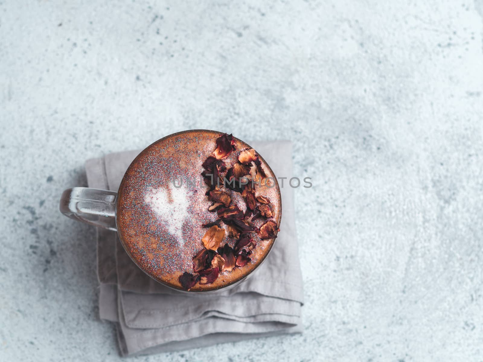 Trendy Coffee with edible glitter and dried rose petals. Cup of sparkly coffee or diamond cappuccino on gray table. Copy space for text. Top view or flat lay.