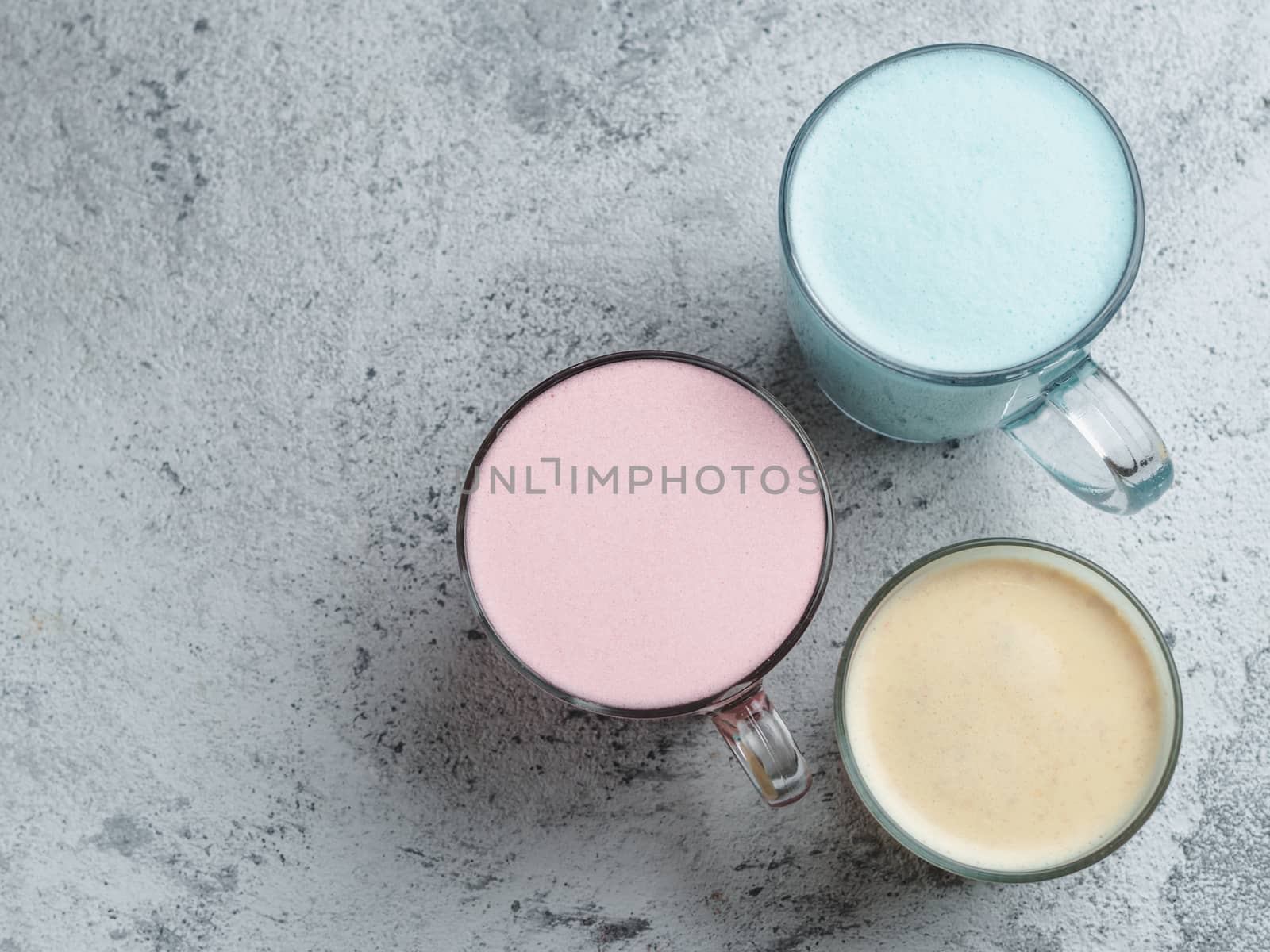 Trendy drinks: Blue, yellow and pink latte. Top view of hot butterfly pea or blue spirulina latte, yellow or gold turmeric latte and pink beetroot latte on gray cement background. Copy space for text