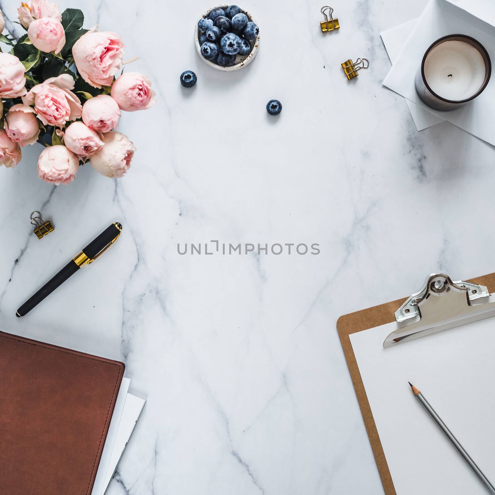 Top view of female home office with copy space in center. Clipboard, flowers, scented candle on white marble. Feminine home office mock up with copy space for text or design. Flat lay