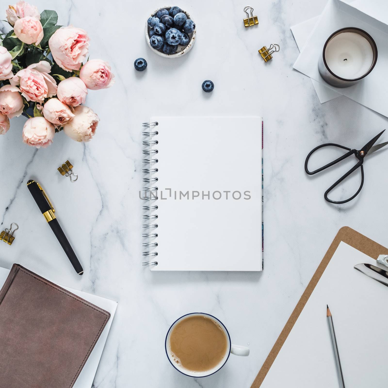 Top view of female home office with copy space in center. Notebook, flowers, scented candle on white marble. Feminine home office mock up with copy space for text or design. Flat lay