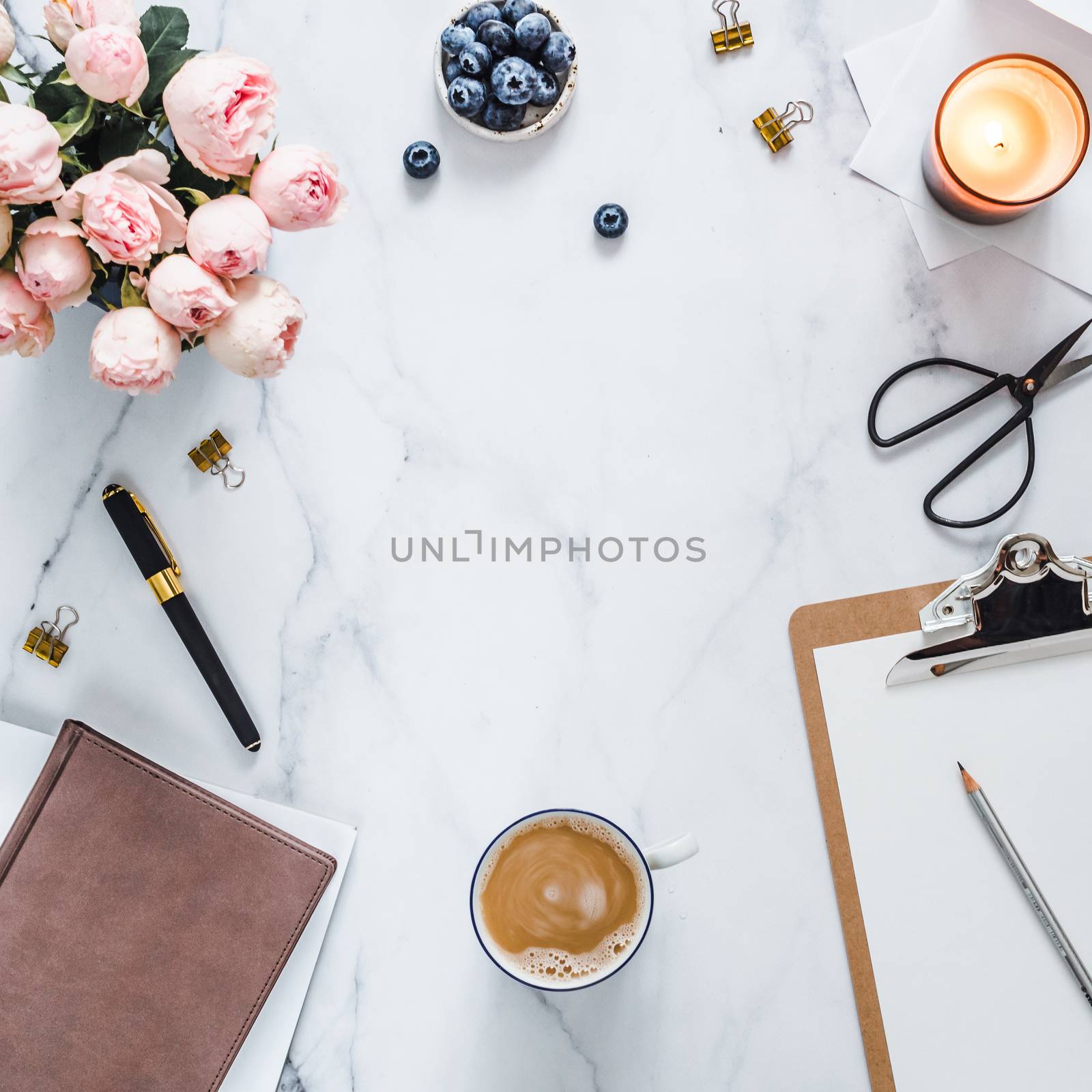 Top view of female home office with copy space in center. Clipboard, flowers, scented candle on white marble. Feminine home office mock up with copy space for text or design. Flat lay